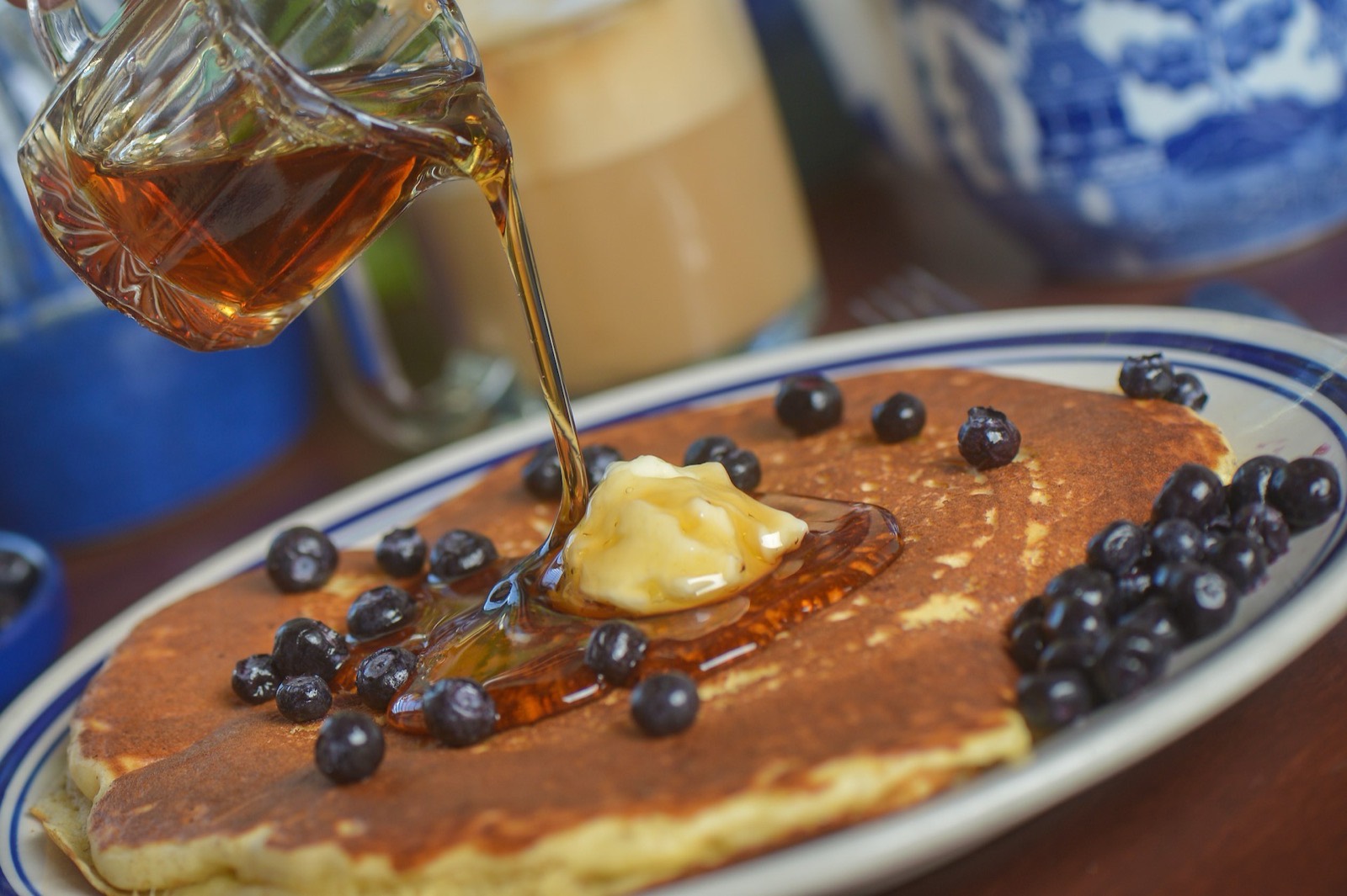 Syrup pouring over a blueberry pancake on blue-and-white Willow china.