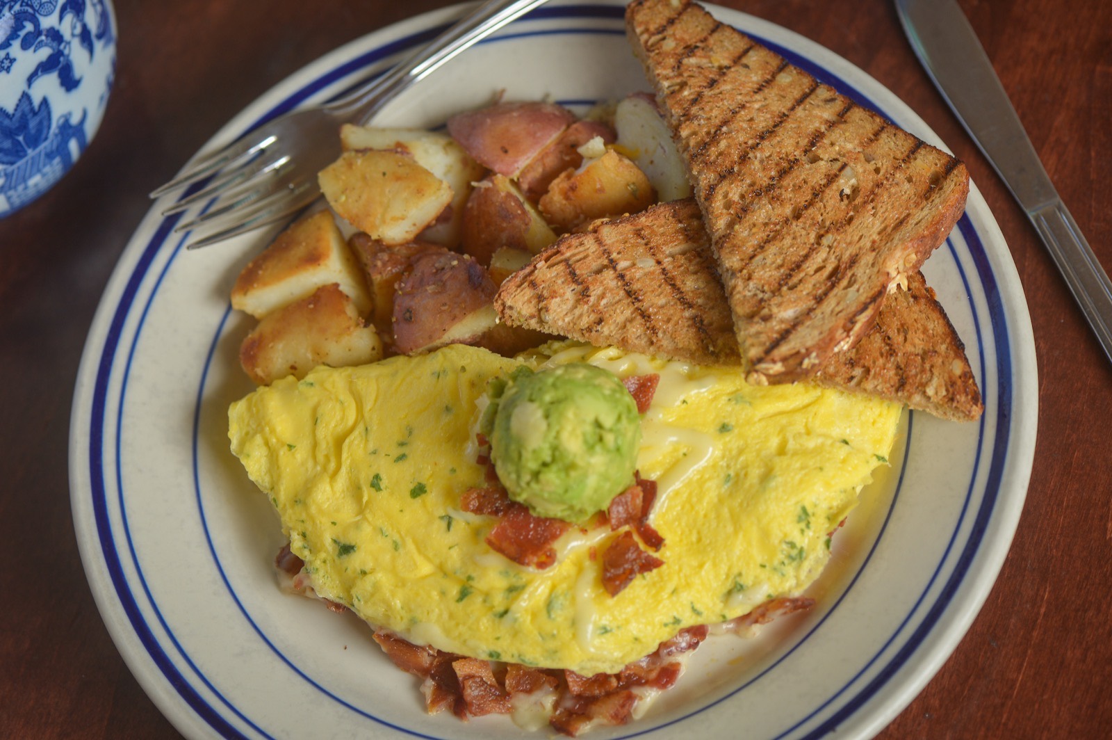 An omelet with bacon and avocado beside grilled wheat toast and red-skin potatoes on Willow china.