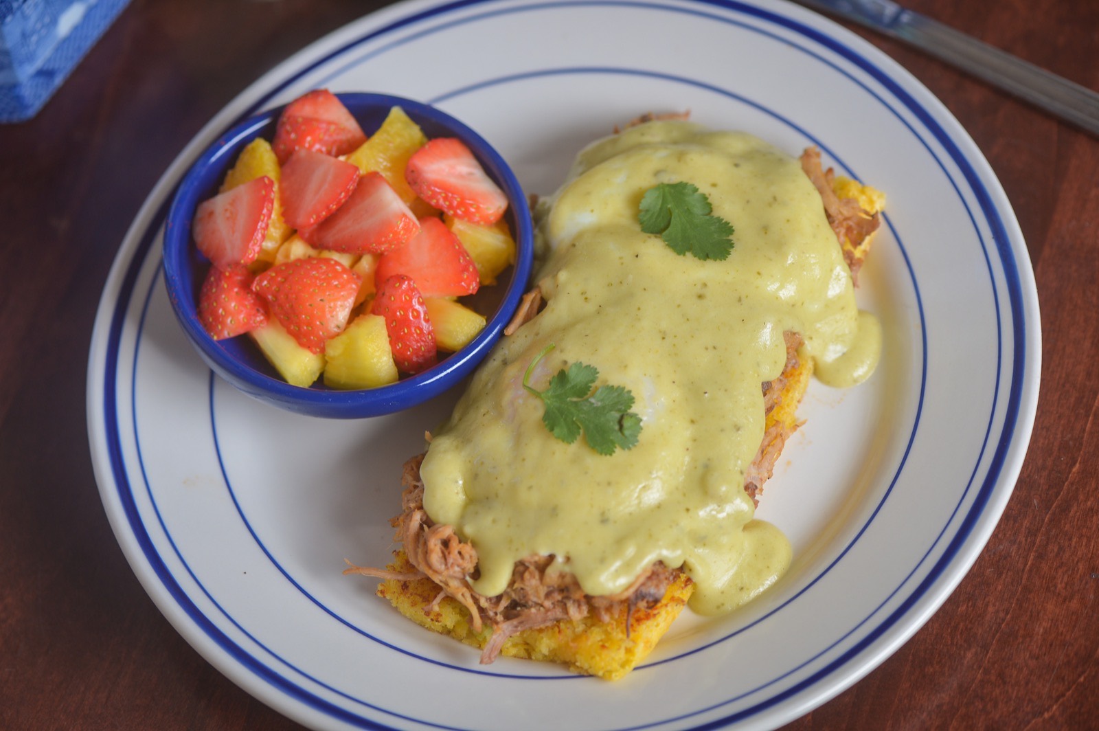 Shredded pork and poached eggs over green chili cornbread under poblano cream sauce, with a fruit cup.