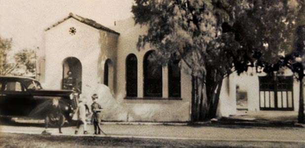A sepia photo of the adobe house in its early days, with a vintage car parked out front.