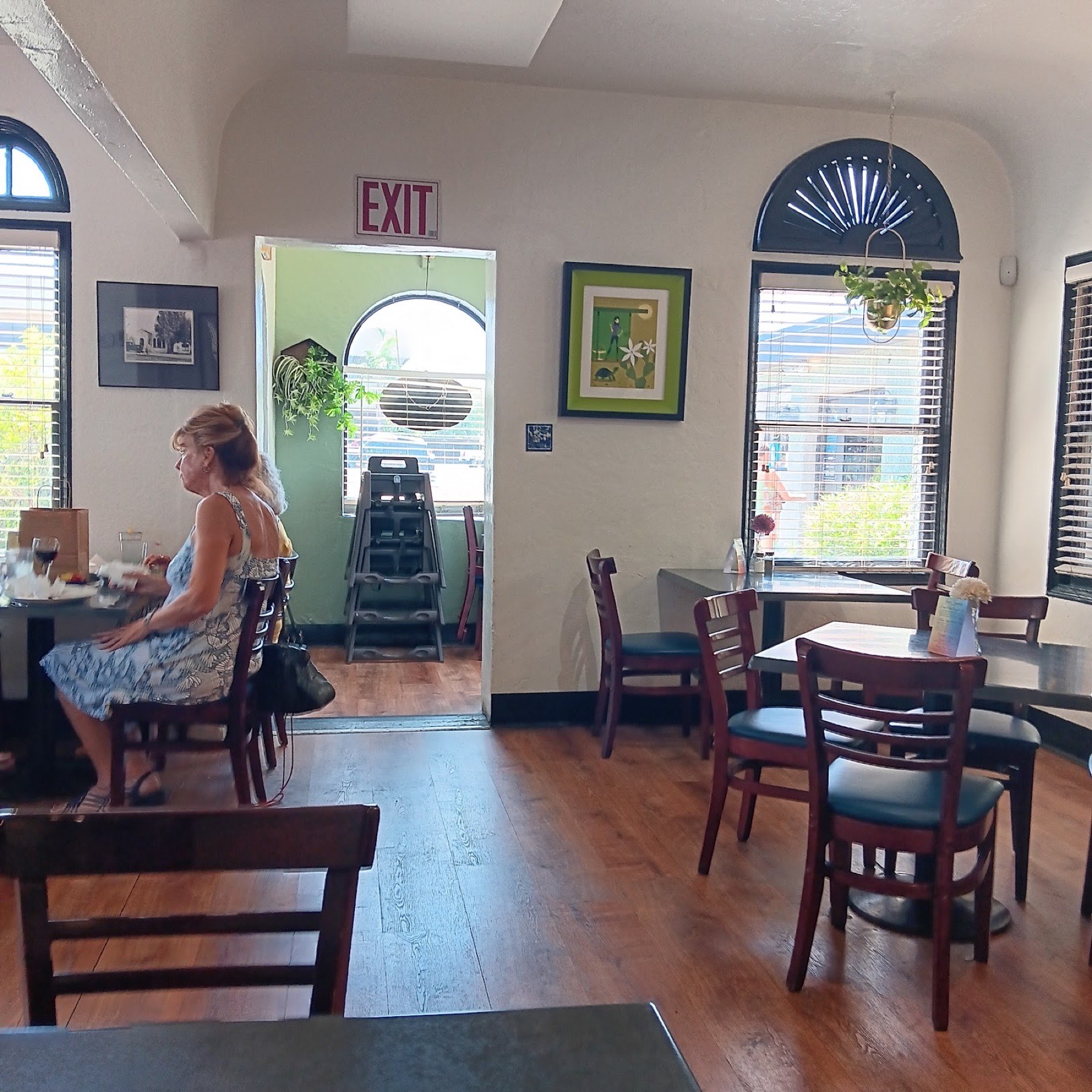 A sunlit dining room with wood floors, arched windows and framed local artwork.