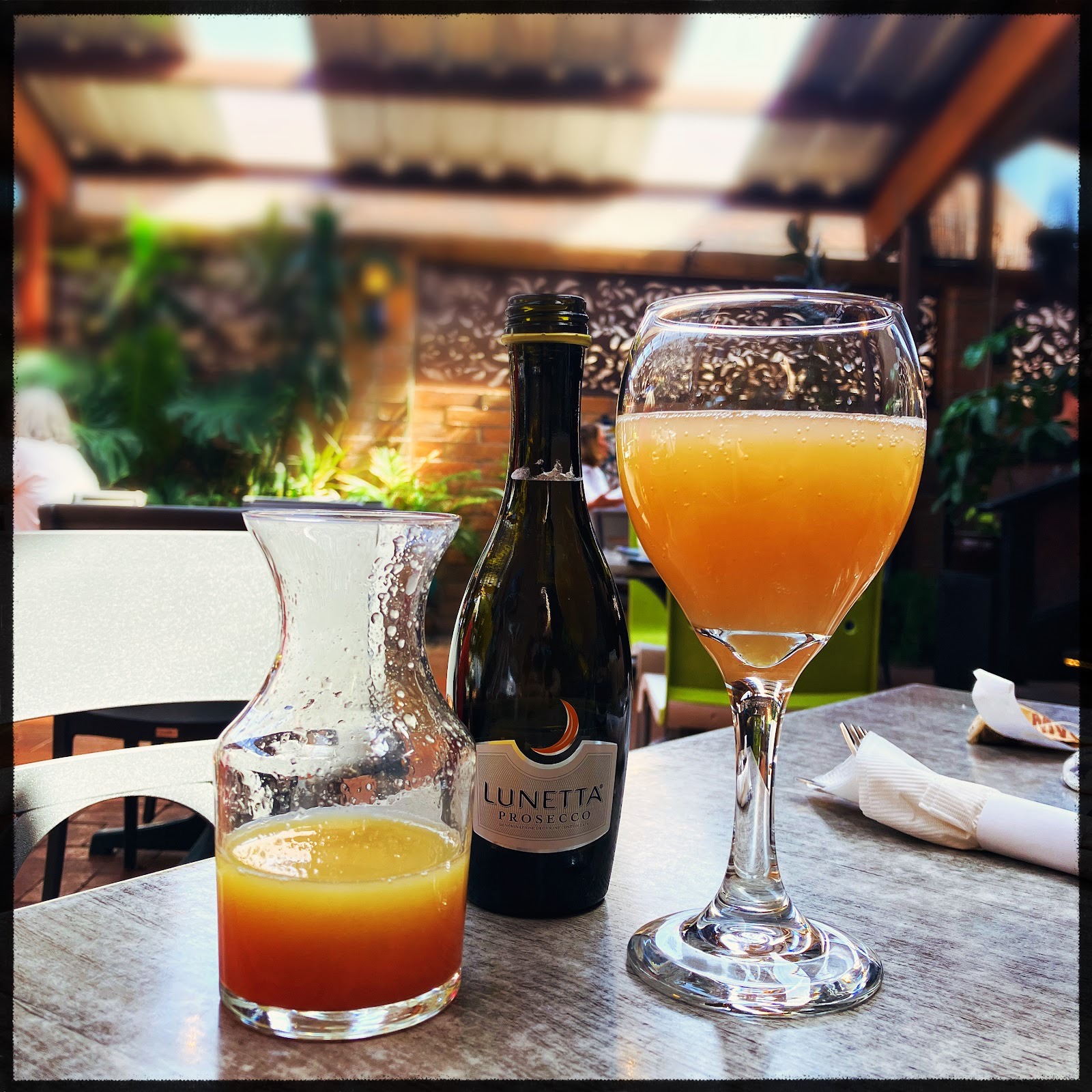A mimosa and a split of prosecco on a patio table in the afternoon light.